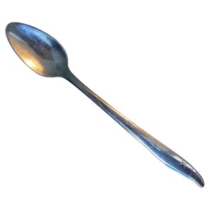 Könnte beinhalten: Ein silberfarbener Metalllöffel mit einer glatten, ovalen Laffe und einem langen, schlanken Stiel. Der Stiel ist mit drei kleinen, eingravierten Sternmustern verziert, die über die Länge verteilt sind und in einem leicht geschwungenen Ende auslaufen.