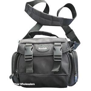 May include: Black Kodak camera bag with a shoulder strap and two side pockets. The bag has two black plastic buckles on the front and a Kodak logo. The bag has a top handle and a padded shoulder strap.