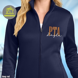 May include: Deep red zip-up jacket with the embroidered text "PTA Kayla" in orange and white. The jacket has a high collar and a zipper closure. The image also includes a small embroidered logo.