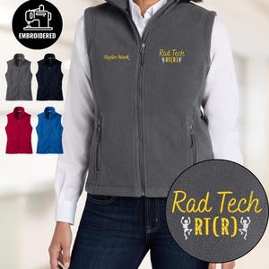 May include: A gray fleece vest with a full zipper, embroidered with "Rad Tech RT(R)" in yellow. The vest has a high collar and two side pockets. Additional vests in navy, red, and blue are shown. The image also includes the word "EMBROIDERED".