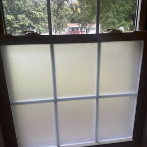 May include: A window with a wooden frame and a grid design. The glass has a frosted effect, and the window is divided into six sections. The view outside shows trees and a house.