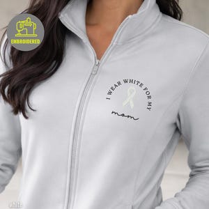 May include: A light gray zip-up jacket with the text "I wear white for my mom" embroidered on the chest. The jacket has a high collar and a zipper closure. The word "Embroidered" is in a circle on the upper left.