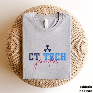 May include: A gray t-shirt with the text "CT TECH jennifer" in blue and pink lettering. A blue and black radiation symbol is above the text.