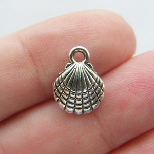 Peut inclure: Breloque en forme de coquille de mer argentée avec un design détaillé. Le breloque a une boucle en haut pour l'attacher à des bijoux ou d'autres objets artisanaux.