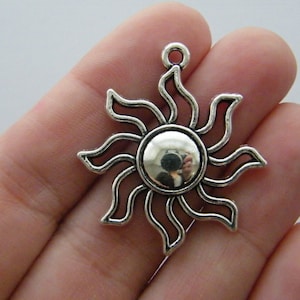 Puede incluir: Colgante de sol de tono plateado con un diseño detallado. El sol tiene un centro redondo y rayos que se extienden hacia afuera.