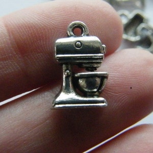 May include: Silver charm in the shape of a stand mixer. The charm is about 2 inches tall and has a loop at the top for attaching to a bracelet or necklace.