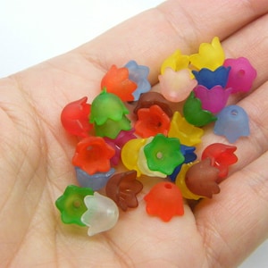 Może przedstawiać: Zbiór kolorowych, przezroczystych plastikowych koralików w kształcie kwiatów. Korale są w różnych odcieniach czerwonego, pomarańczowego, żółtego, zielonego, niebieskiego i fioletowego.