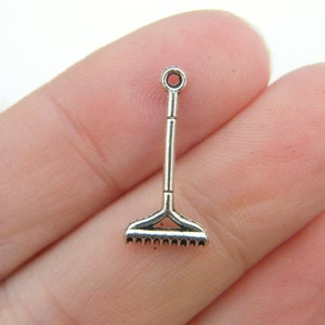 Könnte beinhalten: Silberner Anhänger in Form eines Rechens. Der Rechen hat oben eine Schlaufe zum Anbringen an einem Armband oder einer Halskette.