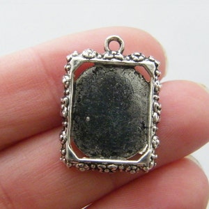Könnte beinhalten: Silberfarbener Anhänger mit einem rechteckigen Rahmen und einem leeren Platz für ein Kamee oder ein Foto. Der Rahmen hat ein dekoratives Blumenmuster.