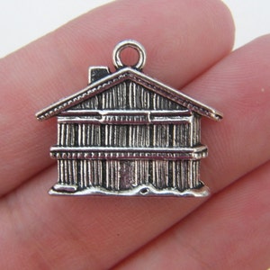 May include: A small, silver-colored house charm with a detailed design. The charm features a pitched roof, chimney, and vertical lines representing the walls. It has a loop at the top for attaching to jewelry or other crafts.