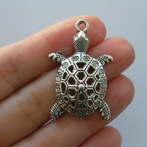 Op de afbeelding: Zilverkleurige schildpadbedel met een gedetailleerd, opengewerkt ontwerp. De bedel heeft een lus aan de bovenkant om aan sieraden of andere knutselwerken te bevestigen.