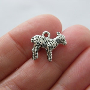 Puede incluir: Encanto de plata de un cordero bebé de pie con una superficie texturizada. El encanto tiene un bucle en la parte superior para sujetarlo a un collar o pulsera.