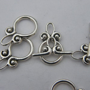 Pu&ograve; includere: Chiusure in metallo argentato con disegni decorativi e piccoli accenti rotondi. Queste chiusure sono utilizzate per la creazione di gioielli e l'artigianato.