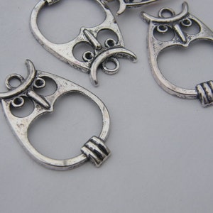 May include: Silver owl charm pendants with a detailed design. The charms have a ring at the top for attaching to jewelry or other crafts.