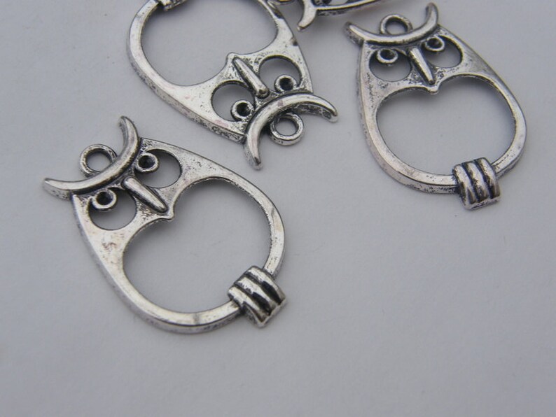 May include: Silver owl charm pendants with a detailed design. The charms have a ring at the top for attaching to jewelry or other crafts.