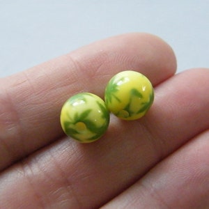 May include: Two yellow and green glass beads with a floral pattern. The beads are round and have a glossy finish.
