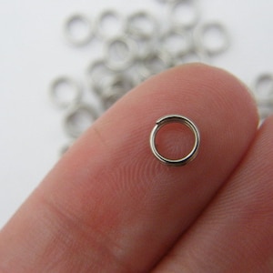 May include: A close-up of a silver jump ring, a type of jewellery finding, held between two fingers. The ring is small and circular, with a smooth, polished finish.