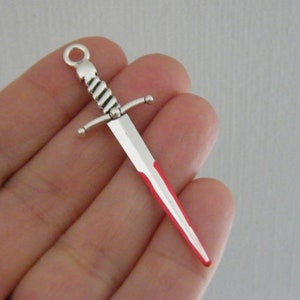 Puede incluir: Encanto de espada de plata con punta roja, perfecto para la elaboración de joyas o proyectos de artesanía.