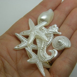 Può includere: Una collezione di ciondoli di vita marina in madreperla bianca, tra cui una stella marina, un cavalluccio marino, una conchiglia e una perla. Questi ciondoli sono perfetti per la creazione di gioielli o per l'artigianato.