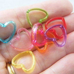 Puede incluir: Surtido de dijes de plástico en forma de corazón de colores. Los dijes son translúcidos y vienen en tonos de azul, verde, amarillo, naranja, rosa y morado.