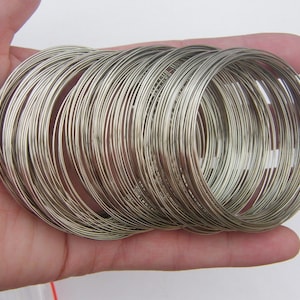 May include: A stack of silver-toned metal bangles, arranged in a circular pattern. The bangles are thin and delicate, and they are all the same size.