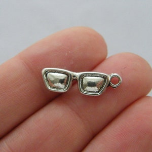May include: Silver-toned charm in the shape of a pair of sunglasses. The charm has a loop at the top for attaching to a necklace or bracelet.