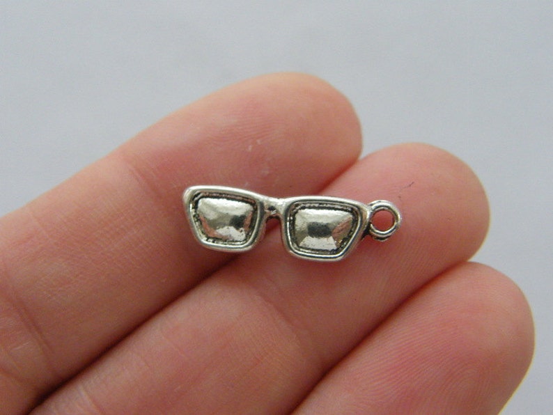 May include: Silver-toned charm in the shape of a pair of sunglasses. The charm has a loop at the top for attaching to a necklace or bracelet.