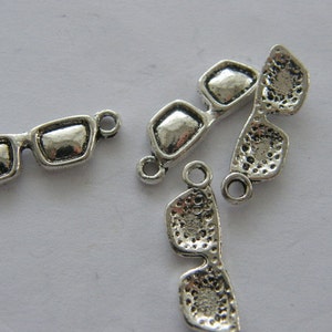 May include: Silver charm pendants in the shape of sunglasses. The charms have a loop at the top for attaching to a bracelet or necklace.