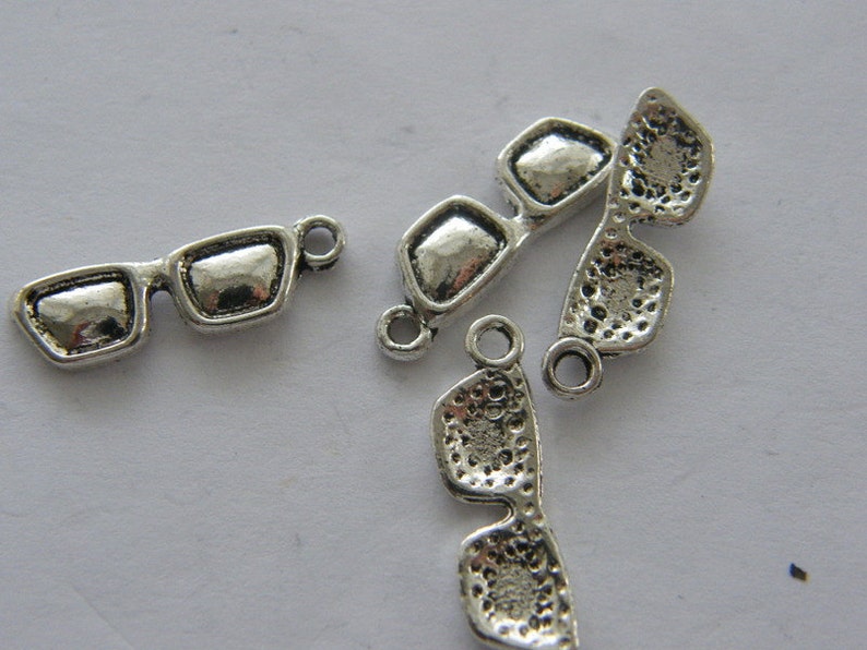 May include: Silver charm pendants in the shape of sunglasses. The charms have a loop at the top for attaching to a bracelet or necklace.