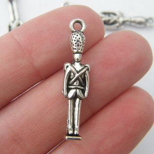 May include: Silver charm of a toy soldier with a tall hat and a crossed-arms pose.