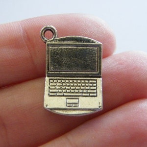 Peut inclure: Un petit charm en forme d'ordinateur portable de style antique, de couleur bronze métallique. Le charm présente un clavier et un écran détaillés, avec une boucle en haut pour l'attacher à un collier ou un bracelet. Le charm est une miniature d'ordinateur.