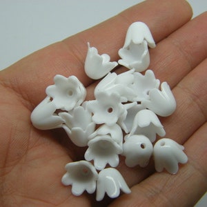 Może przedstawiać: Zbiór białych plastikowych koralików w kształcie kwiatów. Korale mają pięć płatków i mały otwór w środku.
