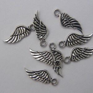 May include: A set of six silver-toned metal angel wing charms with a loop for attaching to jewellery or other crafts.
