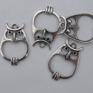 May include: Five silver owl-shaped charms with open loops. The charms have detailed owl faces with large eyes and beaks.