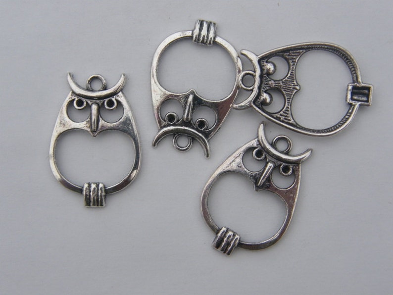 May include: Five silver owl-shaped charms with open loops. The charms have detailed owl faces with large eyes and beaks.