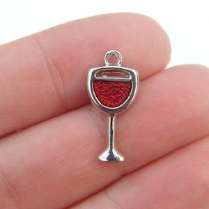 May include: Silver charm shaped like a wine glass with red enamel. The glass is filled with red wine.