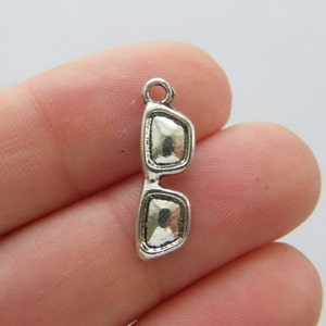 May include: Silver charm in the shape of sunglasses. The charm has a loop at the top for attaching to a bracelet or necklace.