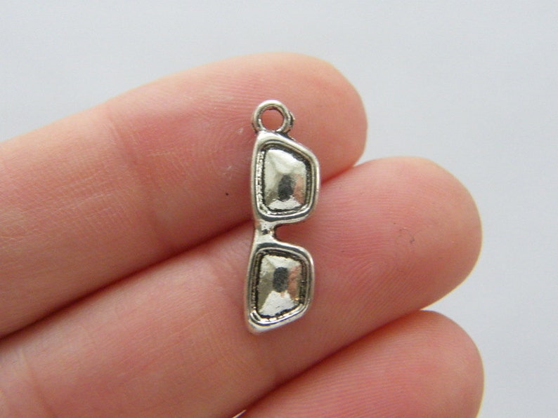 May include: Silver charm in the shape of sunglasses. The charm has a loop at the top for attaching to a bracelet or necklace.