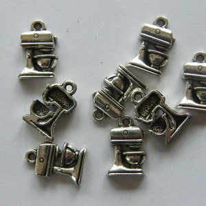 May include: A group of nine silver-toned metal charms shaped like a stand mixer. The charms have a detailed design and are perfect for adding a touch of kitchen-themed charm to jewelry or crafts.
