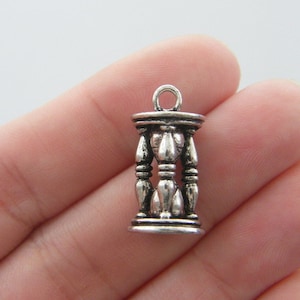 May include: Silver charm in the shape of an hourglass. The charm has a detailed design with a loop at the top for attaching to a necklace or bracelet.
