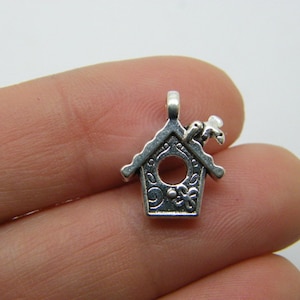 May include: Silver charm in the shape of a birdhouse with a small bird on top. The birdhouse has a round opening and decorative details.