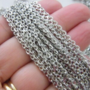 Może przedstawiać: Zbliżenie srebrnego łańcucha, pokazującego poszczególne ogniwa. Łańcuch jest złożony w dłoni, pokazując długość i fakturę łańcucha.