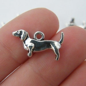 Könnte beinhalten: Silberner Anhänger in Form eines Dackels mit einer Schlaufe zum Anbringen an einer Halskette oder einem Armband.