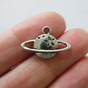 May include: Silver charm with a star and a ring around it, representing a planet with rings.