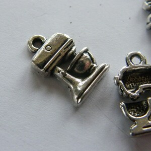 May include: Two silver metal charms shaped like a stand mixer. The charms have a detailed design and are perfect for adding a touch of kitchen-themed charm to jewelry or crafts.