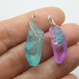 May include: Two crystal pendants with silver wire loops. The pendant on the left is a light blue color and the pendant on the right is a pink and blue color.