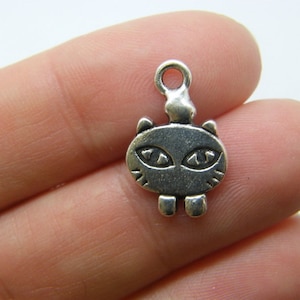 May include: Silver charm in the shape of a cartoon cat with large eyes. The charm has a loop at the top for attaching to a necklace or bracelet.