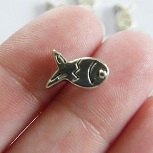 Puede incluir: Encanto de plata en forma de pez. El pez tiene un contorno negro y un patrón ondulado en su cuerpo.