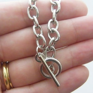 Peut inclure: Un collier en chaîne argentée avec un fermoir à glissière. La chaîne est faite de métal épais et lié.