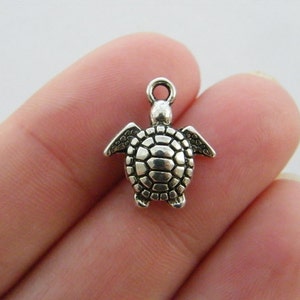 May include: Silver charm in the shape of a turtle with a detailed shell. The charm has a loop at the top for attaching to a necklace or bracelet.